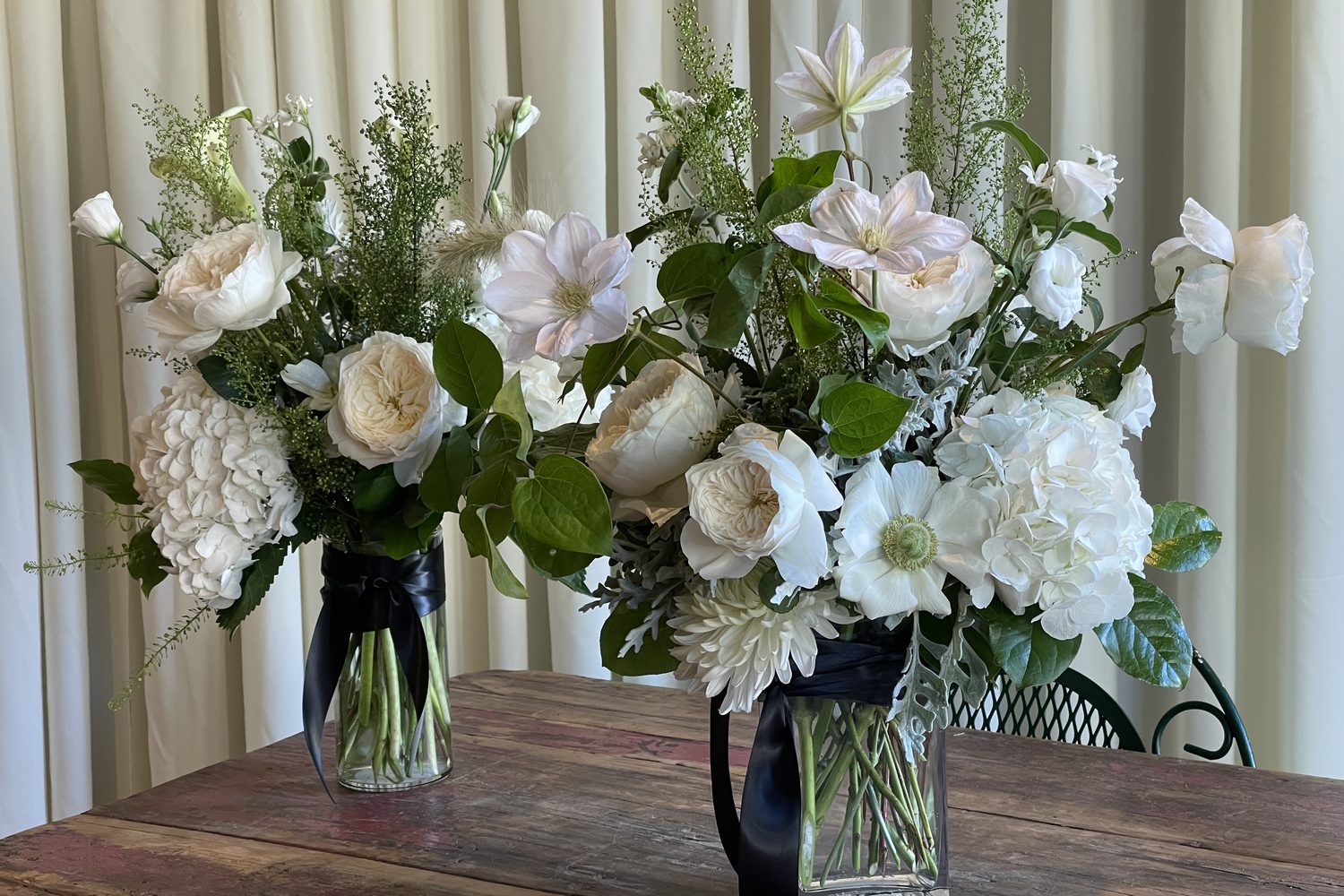 A pair of finished white-and-green arrangements of garden roses, clematis, and hydrangea