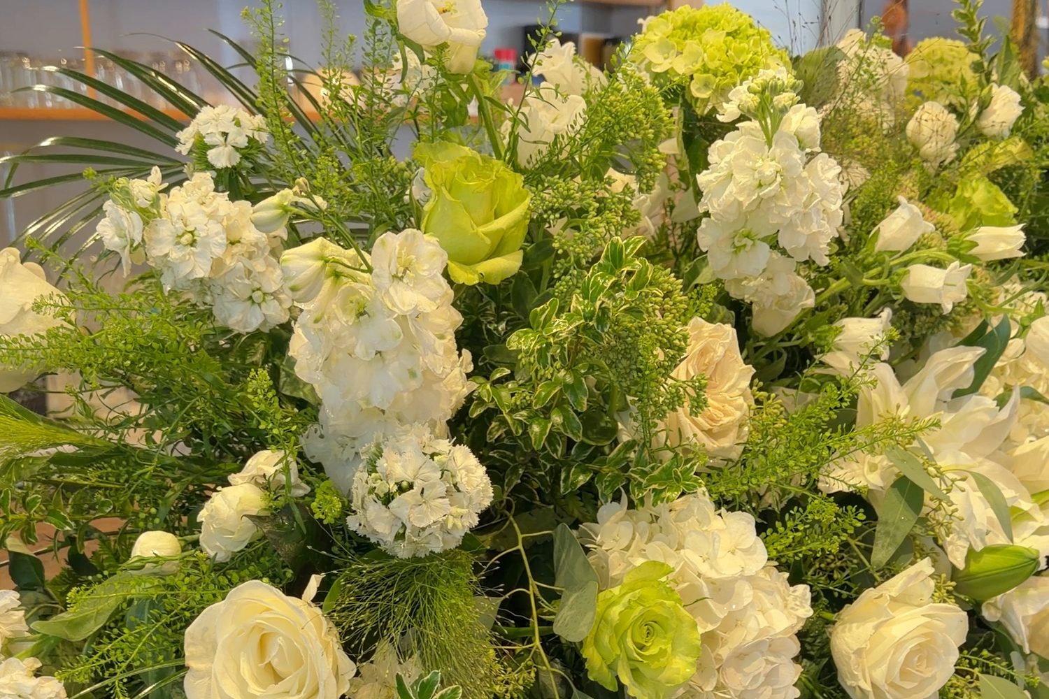 A large white-and-green funeral casket spray of roses, hydrangea, and stock